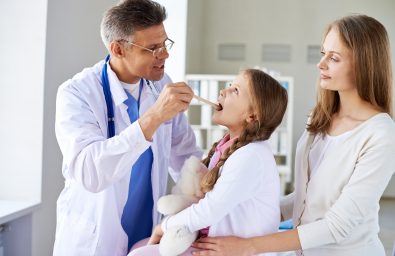 Checking up throat Mature doctor checking up throat of cute girl with her mother near by
